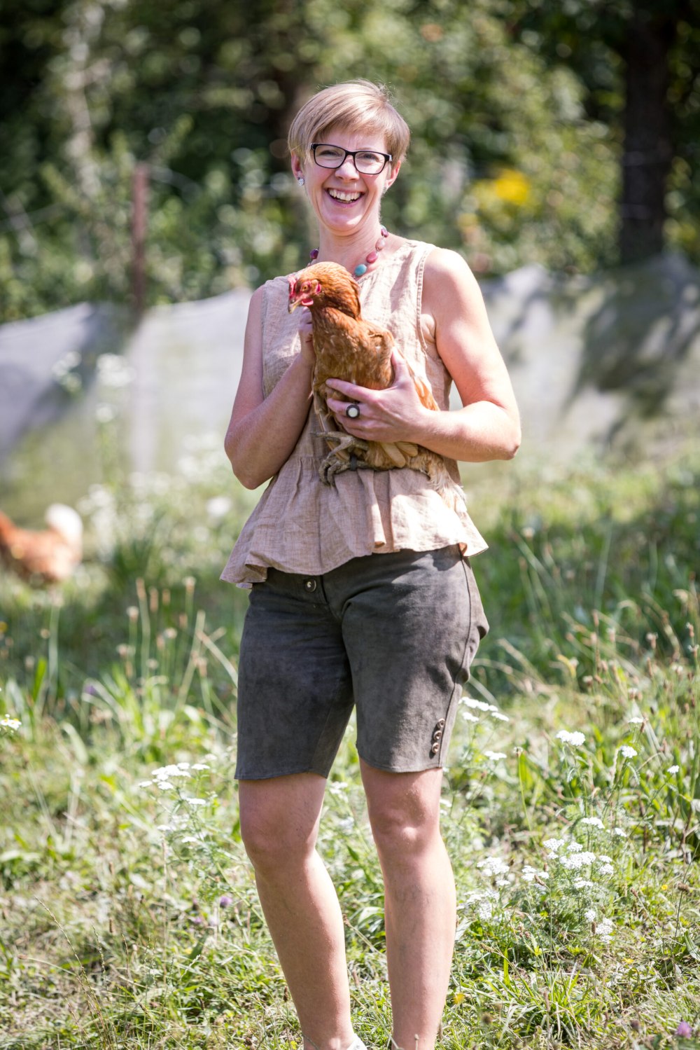 Daniela Huspek mit Huhn in den Händen. Sie lächelt zufrieden an diesem sonnigen Tag.